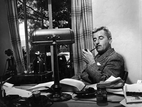 Писатель и сценарист Уильям Фолкнер курит трубку за своим столом в студии Warner Brothers